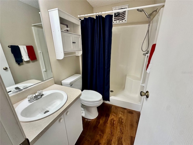 bathroom featuring toilet, a stall shower, vanity, a textured ceiling, and wood finished floors