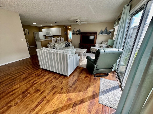 living area featuring a ceiling fan, a textured ceiling, baseboards, and wood finished floors