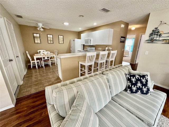 living room featuring a textured ceiling, dark wood-type flooring, visible vents, and recessed lighting