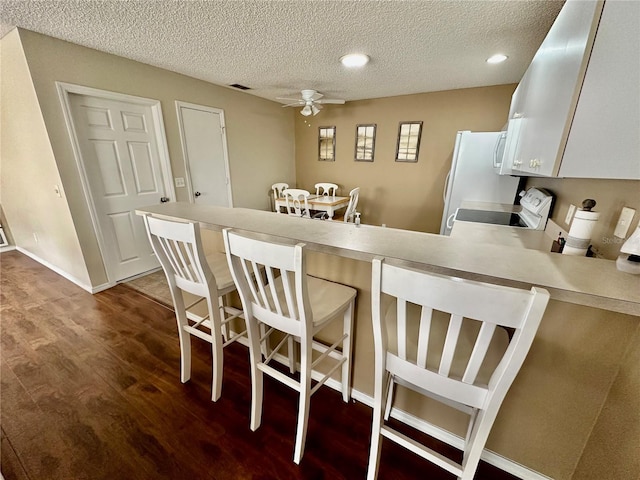 kitchen featuring dark wood finished floors, a breakfast bar area, visible vents, a ceiling fan, and a peninsula