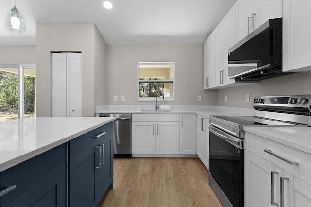 kitchen with stainless steel appliances, light wood-type flooring, white cabinets, and a sink