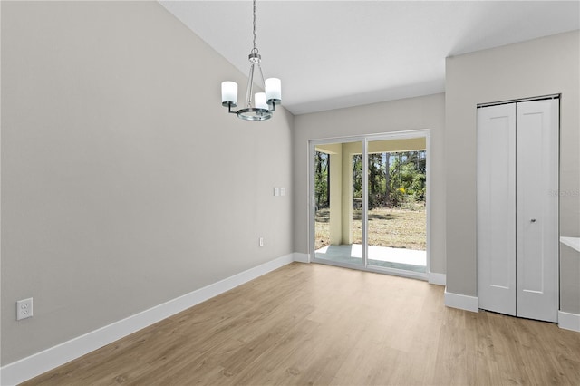 unfurnished dining area featuring light wood-type flooring, a notable chandelier, lofted ceiling, and baseboards