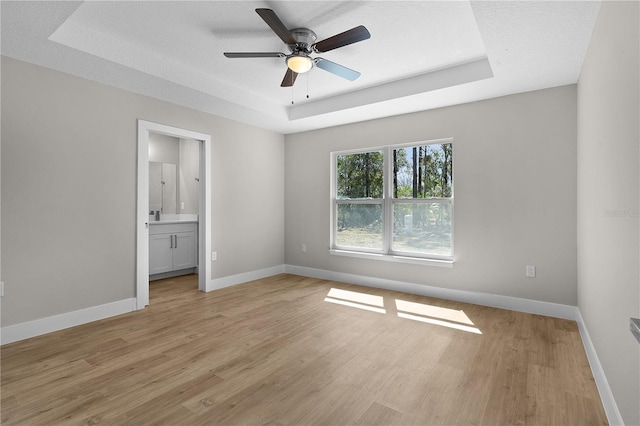 unfurnished bedroom with a tray ceiling, light wood-type flooring, and baseboards