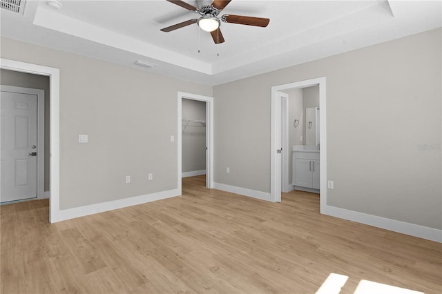 unfurnished bedroom with a tray ceiling, a walk in closet, visible vents, light wood-style flooring, and baseboards