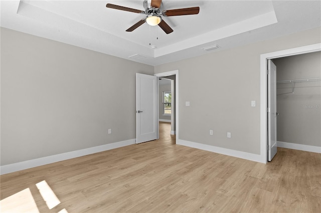 unfurnished bedroom with light wood finished floors, baseboards, and a raised ceiling