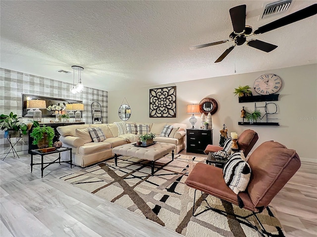living area featuring light wood finished floors, wallpapered walls, a ceiling fan, and visible vents