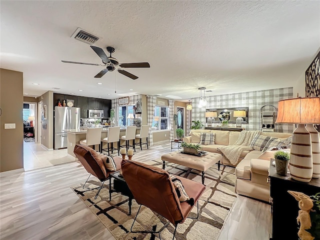 living room with baseboards, a ceiling fan, visible vents, and a wealth of natural light