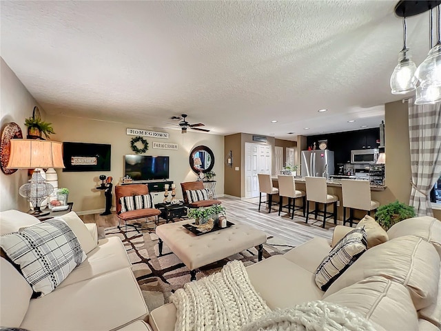 living area with baseboards, a ceiling fan, a textured ceiling, and recessed lighting