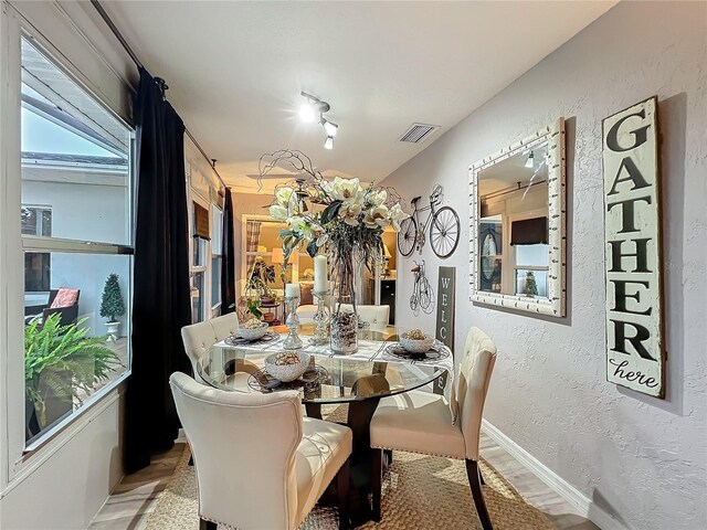 dining space featuring a textured wall, visible vents, baseboards, and wood finished floors