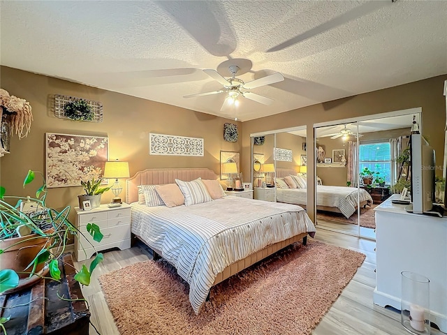 bedroom with two closets, ceiling fan, a textured ceiling, and light wood-type flooring