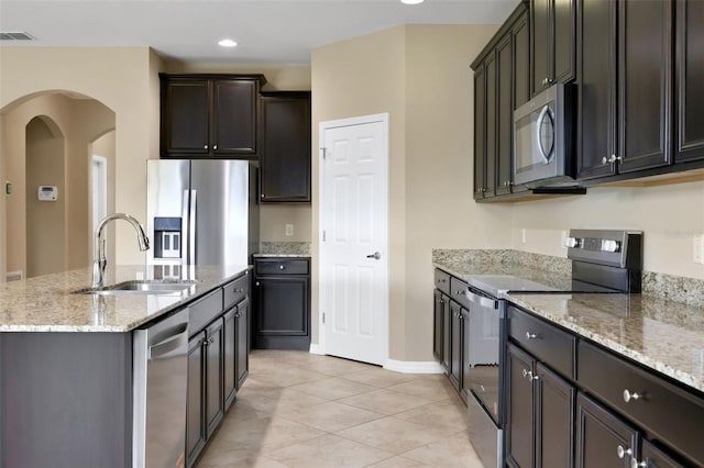 kitchen with arched walkways, visible vents, an island with sink, stainless steel appliances, and a sink