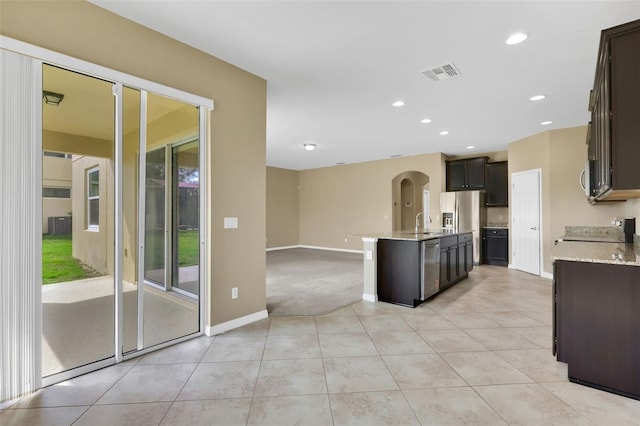 kitchen with a center island with sink, visible vents, dark brown cabinets, a sink, and light tile patterned flooring