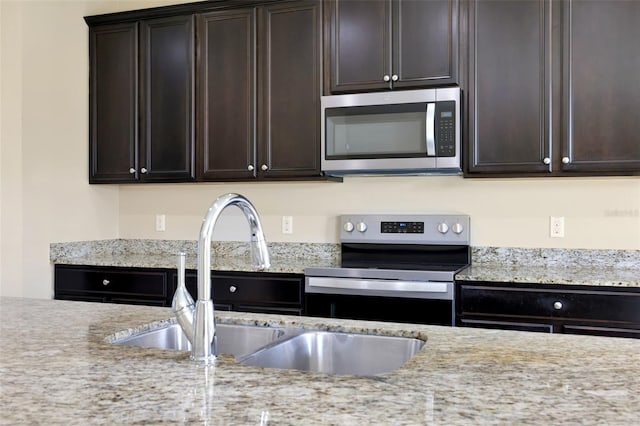 kitchen featuring stainless steel appliances, a sink, light stone counters, and dark brown cabinets