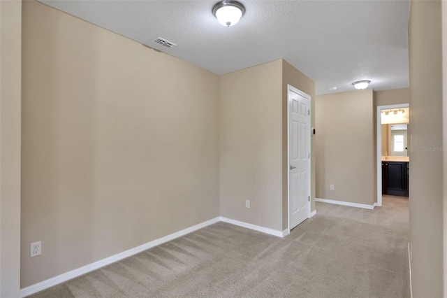 unfurnished room with light carpet, visible vents, baseboards, and a textured ceiling