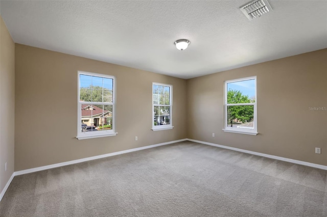 carpeted empty room with a healthy amount of sunlight, baseboards, visible vents, and a textured ceiling