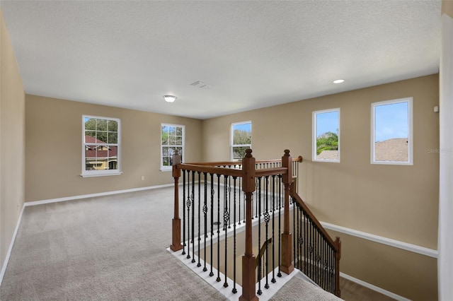 hall with baseboards, carpet flooring, a textured ceiling, and an upstairs landing