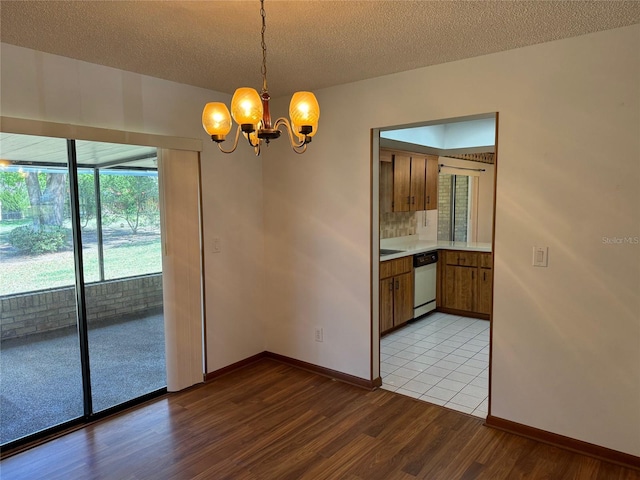 unfurnished dining area with light wood-type flooring, a notable chandelier, baseboards, and a textured ceiling