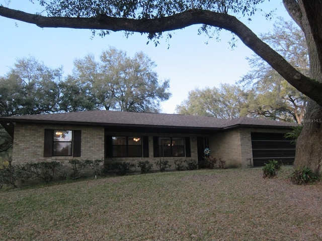 single story home featuring a front yard, brick siding, and a shingled roof