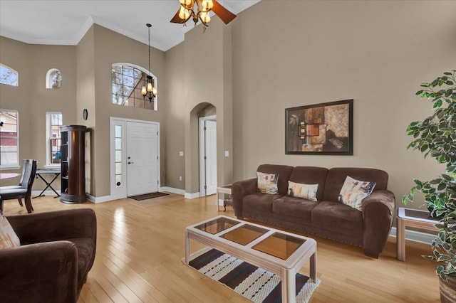 living area featuring baseboards, arched walkways, crown molding, light wood-type flooring, and a notable chandelier