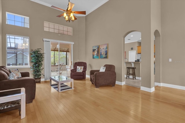 living area featuring light wood-style floors, arched walkways, crown molding, and baseboards