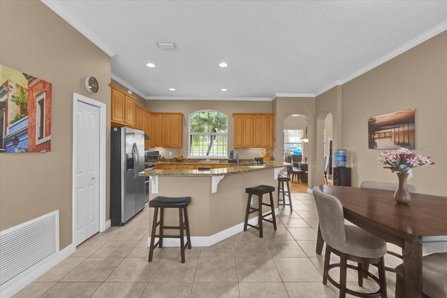 kitchen with arched walkways, stainless steel refrigerator with ice dispenser, visible vents, ornamental molding, and light tile patterned flooring