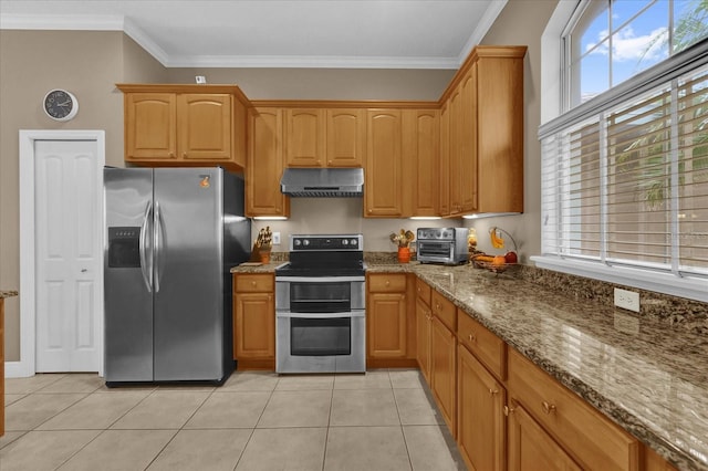 kitchen featuring crown molding, stainless steel appliances, light tile patterned flooring, wall chimney range hood, and dark stone countertops