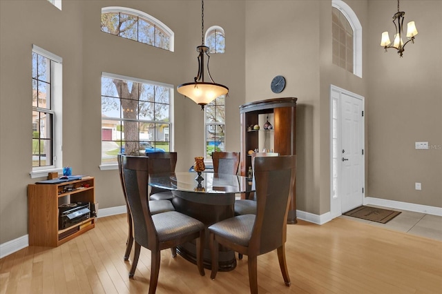 dining space with light wood-type flooring, a high ceiling, baseboards, and a notable chandelier