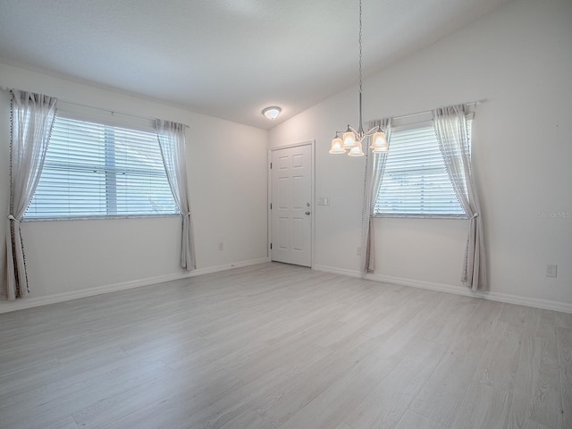 spare room with lofted ceiling, a healthy amount of sunlight, light wood-style flooring, and an inviting chandelier