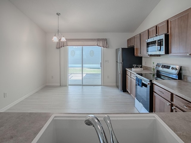 kitchen with pendant lighting, stainless steel appliances, light wood-style floors, vaulted ceiling, and a sink