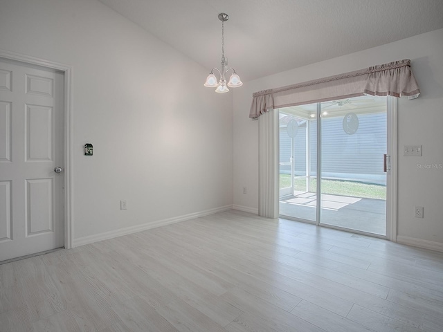 empty room featuring a chandelier, lofted ceiling, baseboards, and wood finished floors