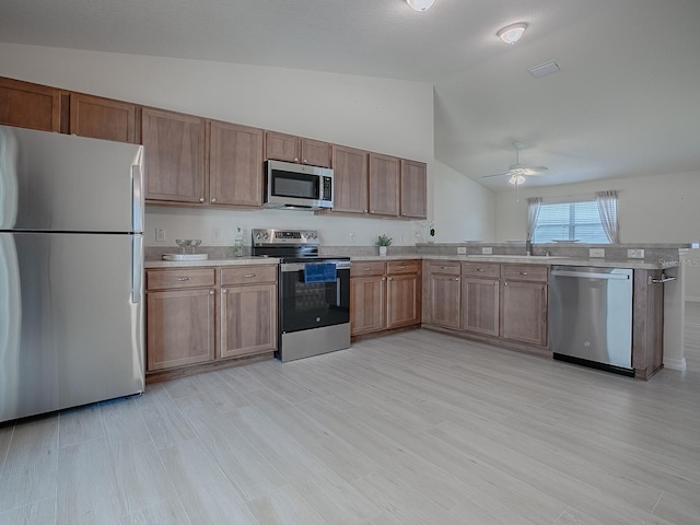 kitchen with ceiling fan, a peninsula, vaulted ceiling, stainless steel appliances, and light countertops