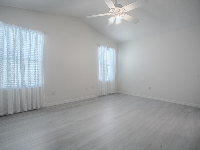 spare room with lofted ceiling, light wood-type flooring, baseboards, and a ceiling fan