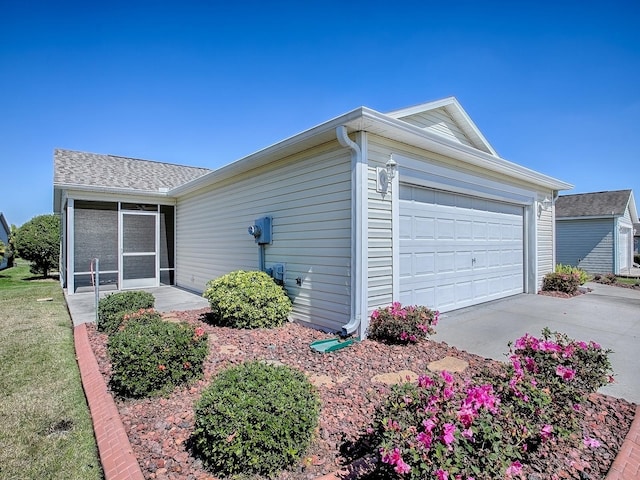 ranch-style house featuring an attached garage, a sunroom, a shingled roof, and concrete driveway