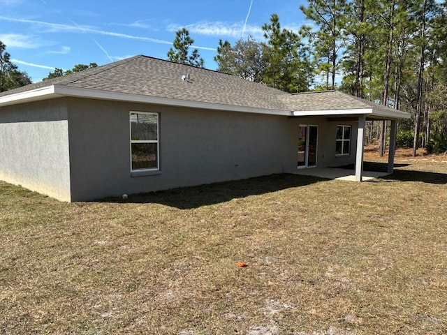 rear view of house with roof with shingles, a lawn, and stucco siding