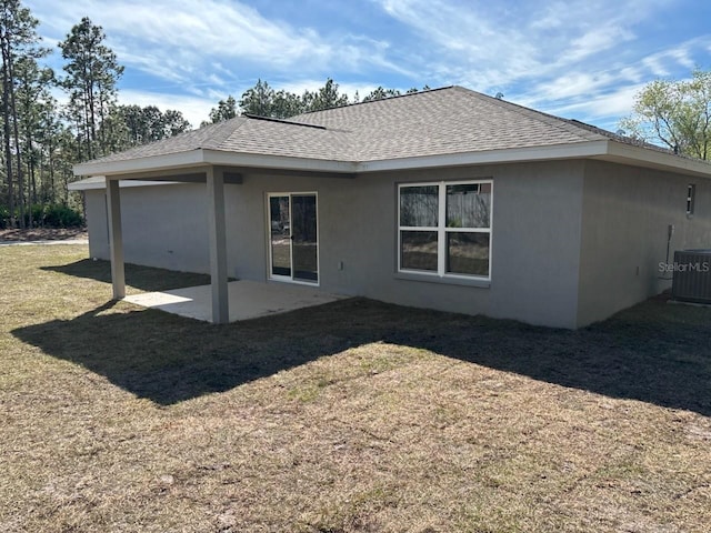 rear view of property featuring roof with shingles, stucco siding, a lawn, central AC unit, and a patio area