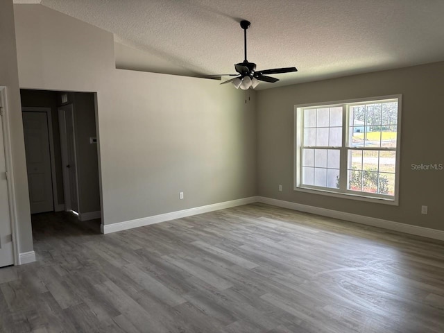 empty room featuring lofted ceiling, ceiling fan, baseboards, and wood finished floors