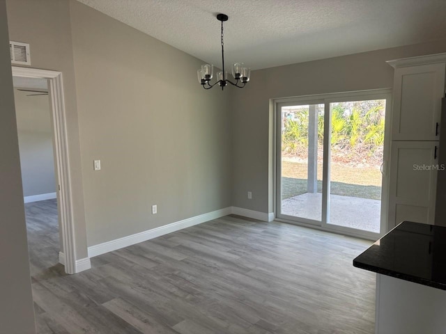 unfurnished dining area featuring light wood-type flooring, baseboards, a chandelier, and a textured ceiling