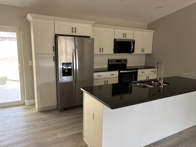 kitchen with appliances with stainless steel finishes, dark countertops, a sink, and white cabinetry