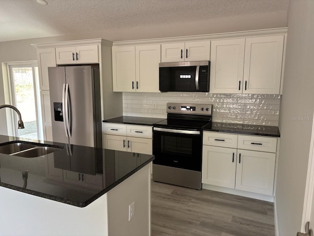 kitchen featuring stainless steel appliances, wood finished floors, a sink, white cabinets, and backsplash