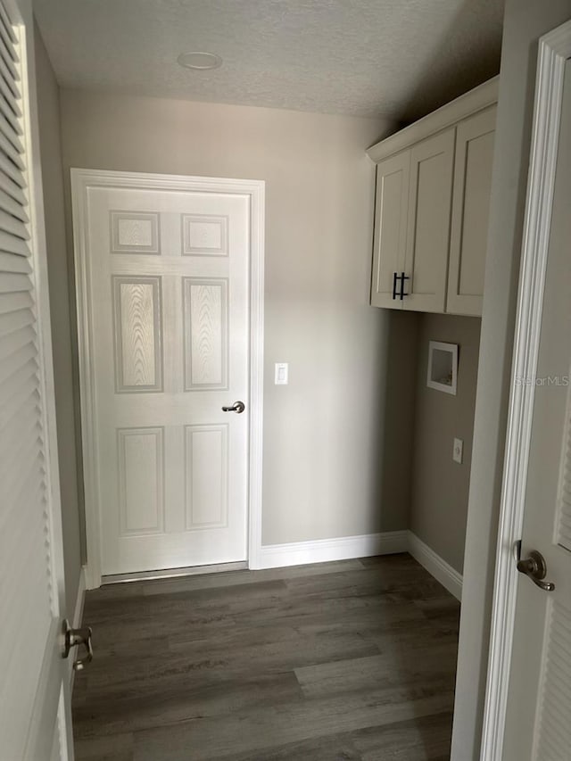 washroom with a textured ceiling, hookup for a washing machine, dark wood-type flooring, baseboards, and cabinet space