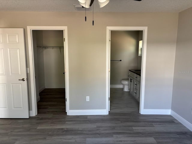 unfurnished bedroom with a textured ceiling, a spacious closet, a closet, and baseboards