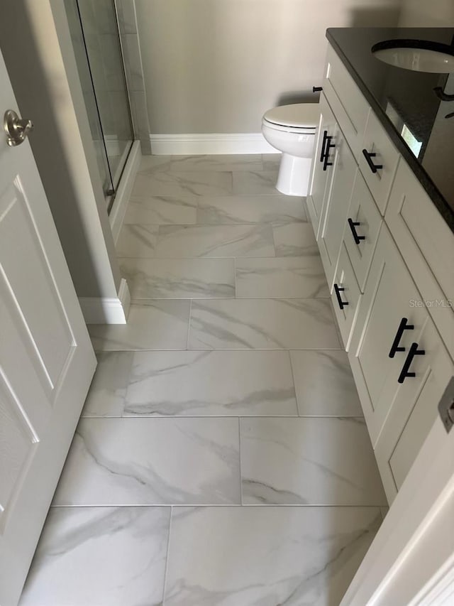 full bathroom featuring marble finish floor, toilet, a shower stall, vanity, and baseboards