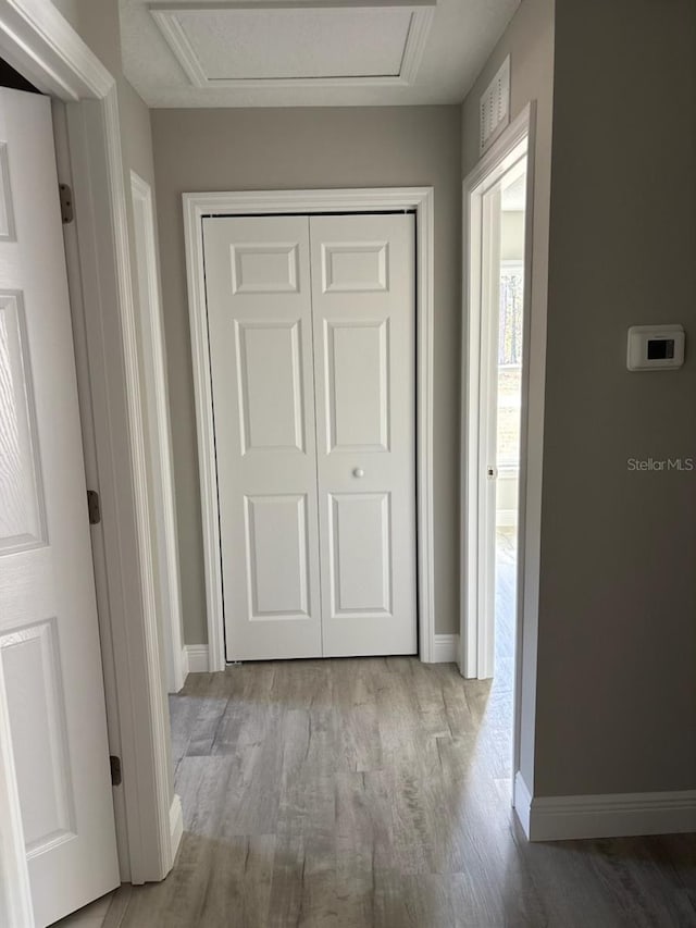 hall featuring attic access, light wood-type flooring, and baseboards