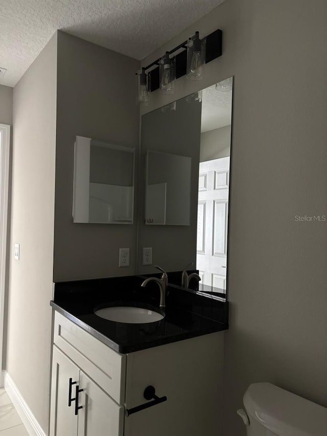 bathroom featuring toilet, baseboards, a textured ceiling, and vanity