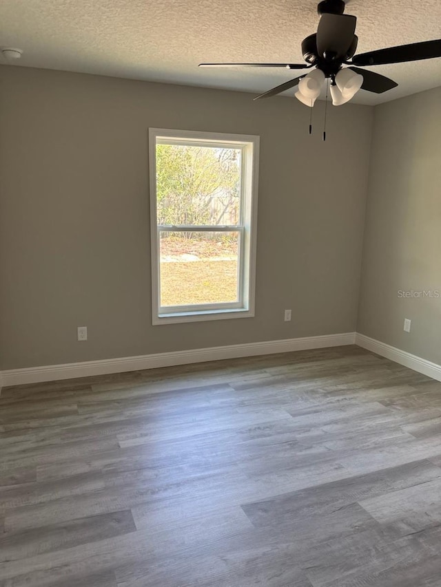 empty room with a ceiling fan, a textured ceiling, baseboards, and wood finished floors