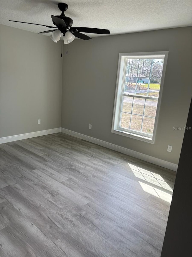 empty room with ceiling fan, a textured ceiling, baseboards, and wood finished floors