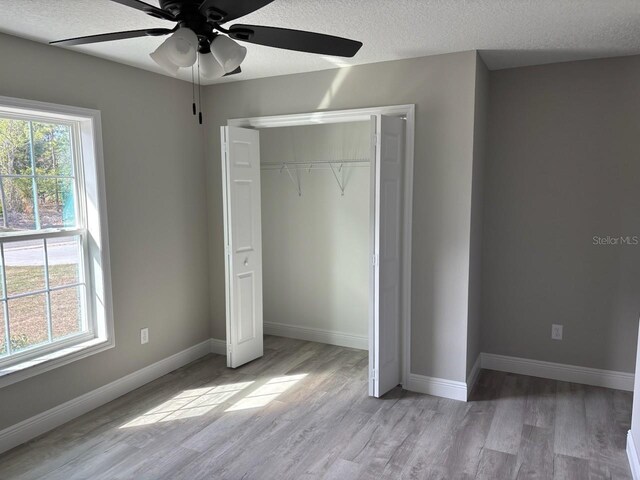 unfurnished bedroom with baseboards, a textured ceiling, a closet, and light wood-style floors