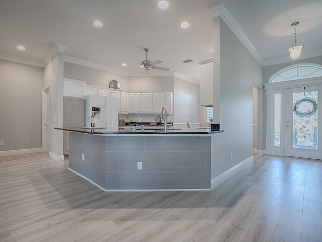 kitchen featuring decorative backsplash, dark countertops, white fridge with ice dispenser, white cabinetry, and a sink