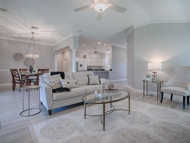 living area featuring crown molding, ornate columns, light wood-style floors, baseboards, and ceiling fan with notable chandelier