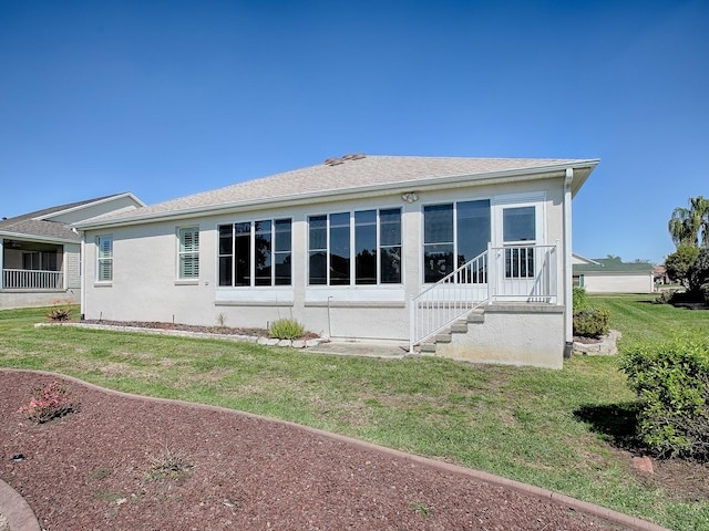 back of house featuring roof with shingles, a lawn, and stucco siding